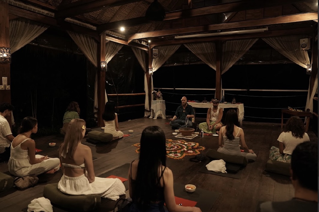 Evening group ceremony in an open-air wooden pavilion with a flower mandala