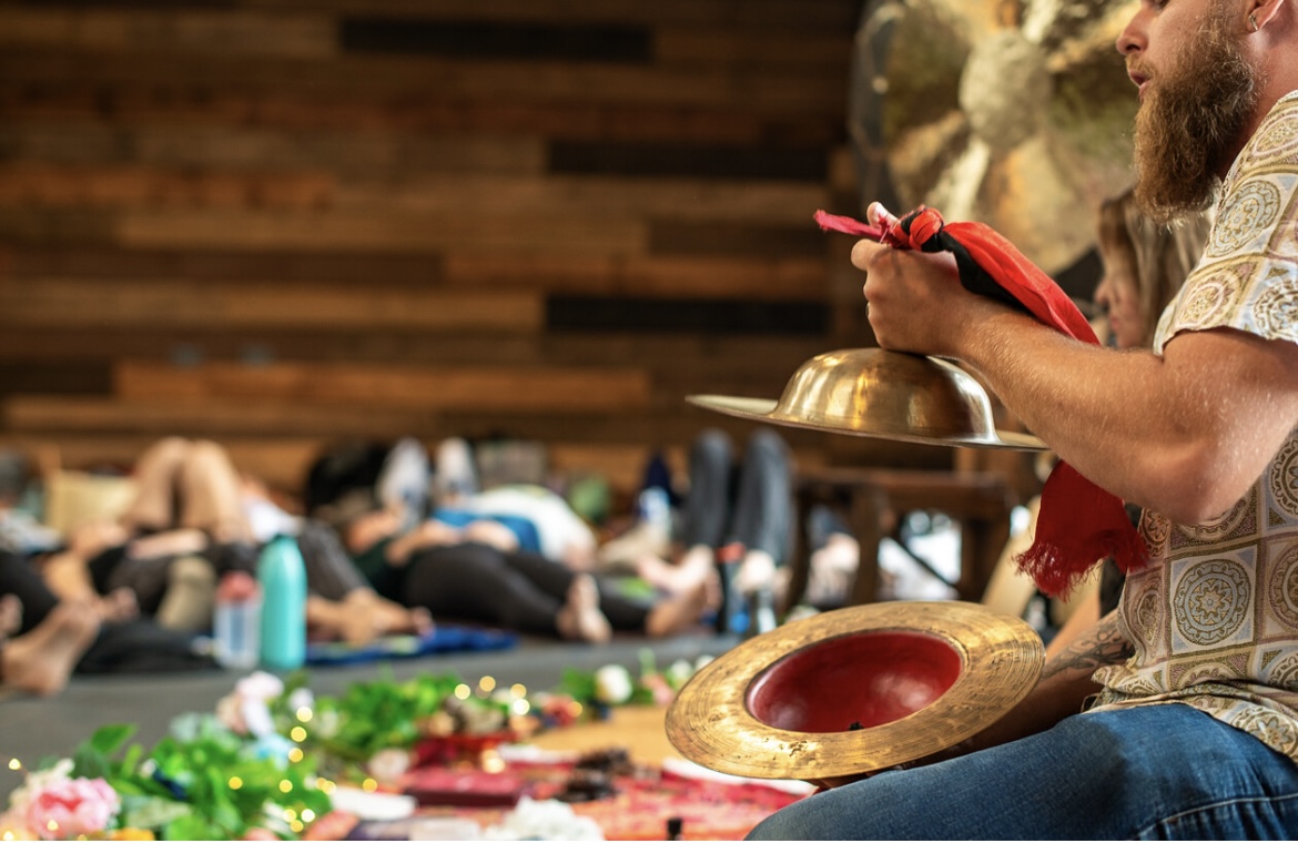 Practitioner sounding brass cymbals during a sound bath
